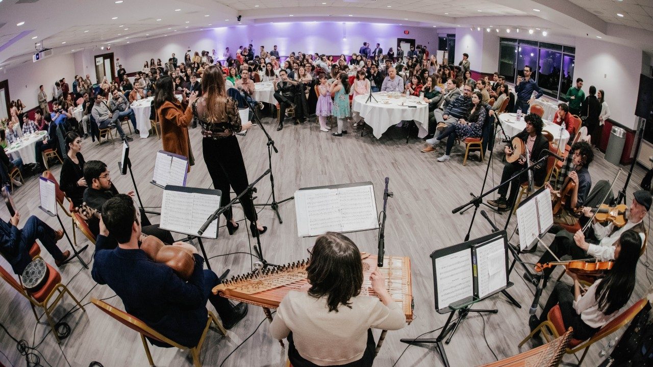  The Itraab Arabic Music Ensemble performs for Persian New Year. A large crowd watches from tables. The photo was taken with a wide angle lens from behind the musicians.