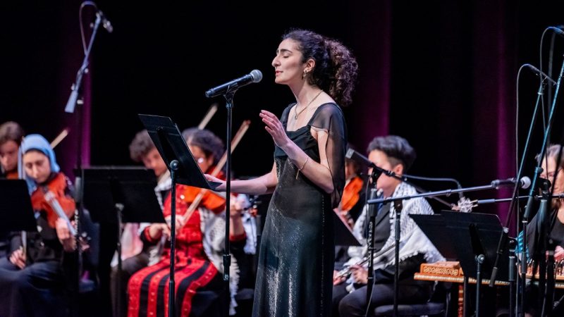 A member of the Itraab Arabic Music Ensemble, a young woman with curly brown hair pulled back into a ponytail and wearing a black dress, performs during the ensemble's spring 2024 concert at the Moss Arts Center.