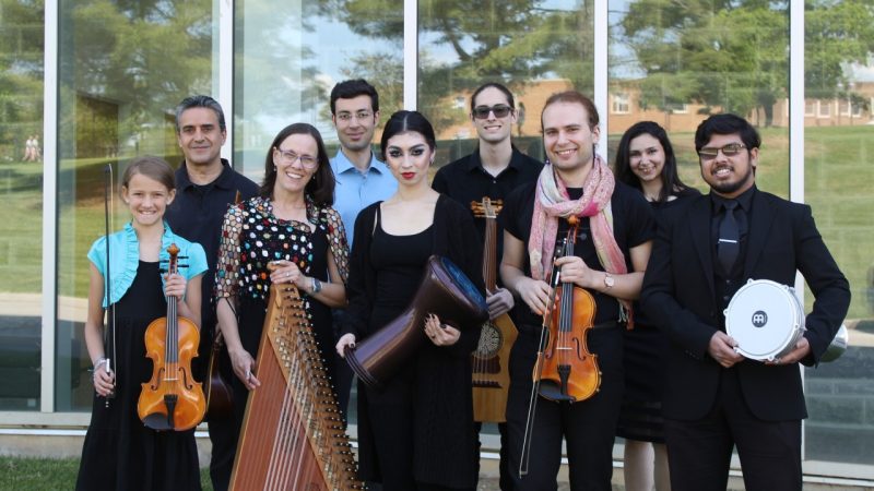 Members of the Itraab Arabic Music Ensemble wear concert attire and hold their instruments in front of the exterior windows at the Moss Arts Center.