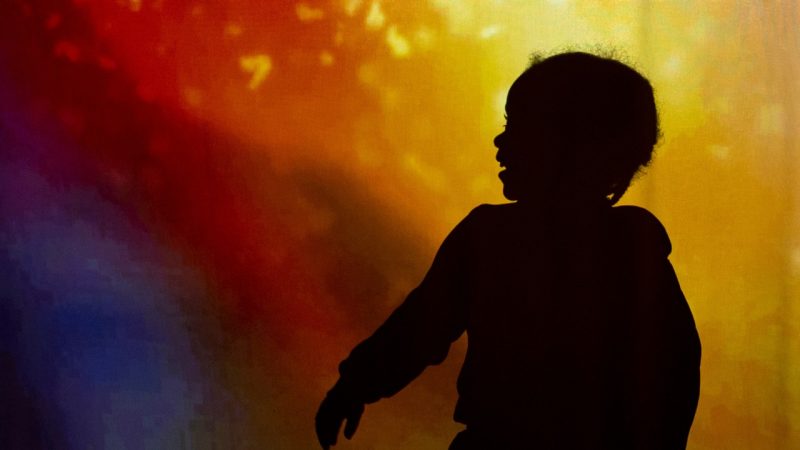  A silhouette of a young boy in front of a brightly colored background. He is smiling widely.