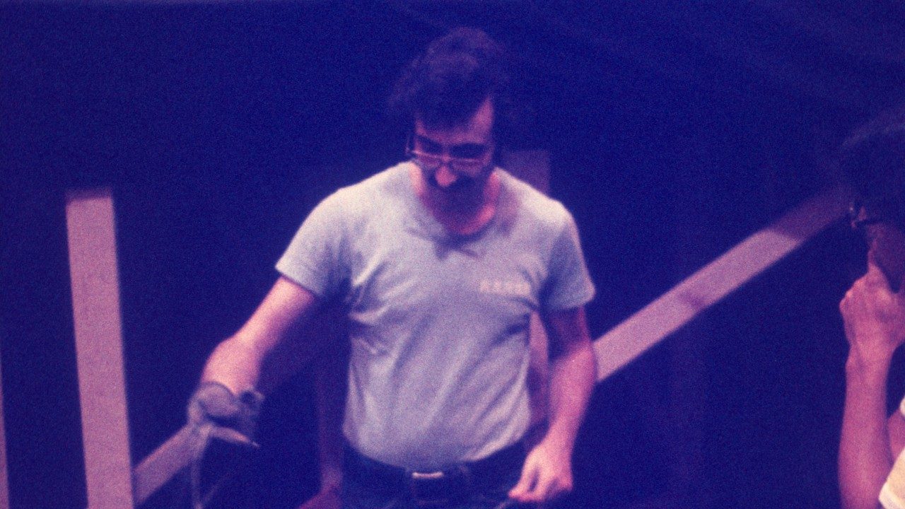  A member of the New Virginians holds a cable. He's a white man with glasses, dark brown hair, and a dark brown moustache, wearing a light blue t-shirt and black belt.