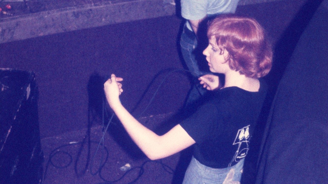  A member of the tech crew of the New Virginians wrangles a cable. She is a white woman with shiny medium length red hair, wearing a black t-shirt.