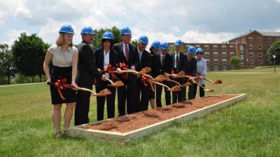 Ten Virginia Tech and state officials hold scoops of dirt in gold shovels and wear blue hard hats on the site of the Moss Arts Center.