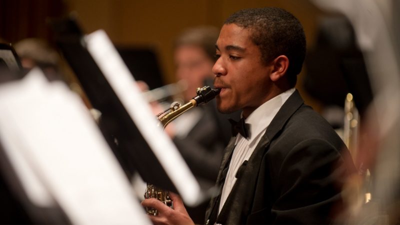  A School of Performing Arts student, a Black man with short hair and a short goatee in a tuxedo, performs in the Wind Ensemble