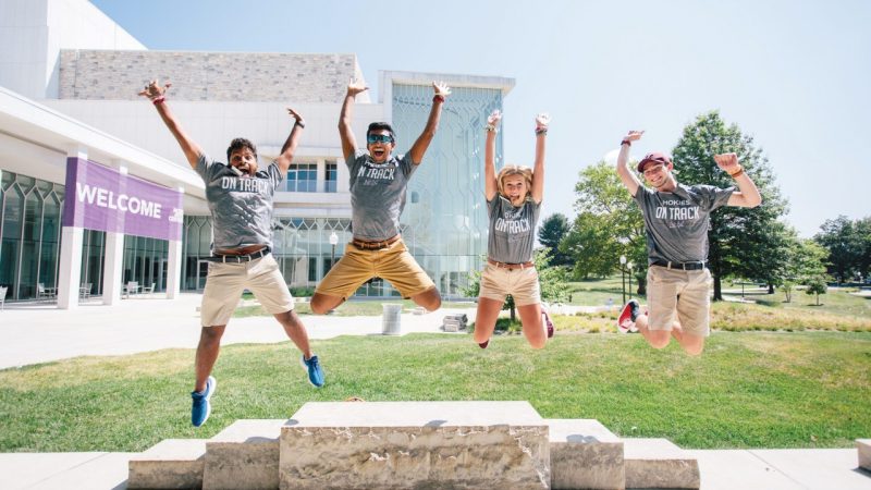 Virginia Tech students jump for joy from a stone bench out front of the Moss Arts Center