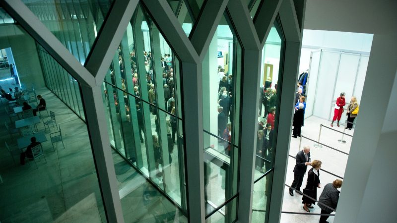  Image of the Moss Arts Center's grand lobby through the honeycomb windows. Lobby is busy and full for a performance.